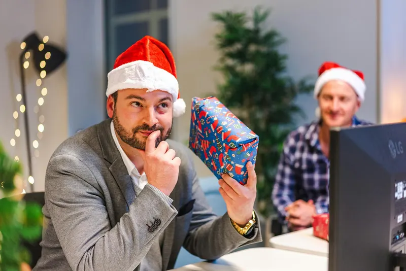 Man in Santa hat contemplating gift during office Christmas celebration.